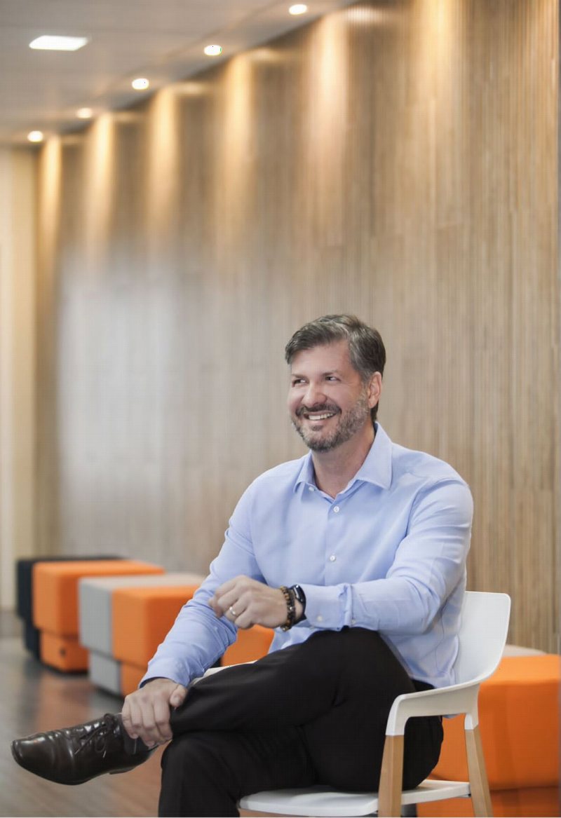 Gui Gatti sentado, de camisa azul, sorrindo